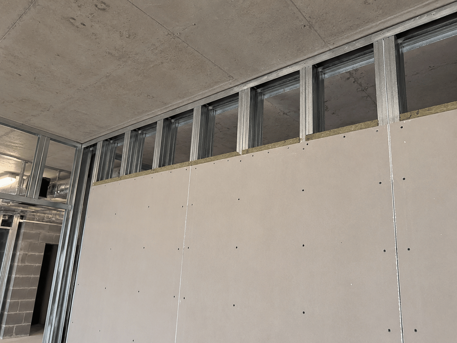 Fire-rated metal stud partition wall installation with fire-resistant boards and deflection head detail within a commercial construction environment.