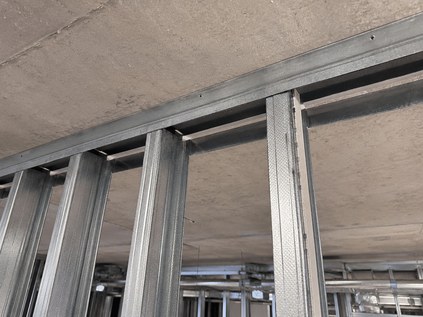 Close-up of a metal stud partition head detail with deflection head strip installed beneath a concrete soffit in a commercial interior fit-out.